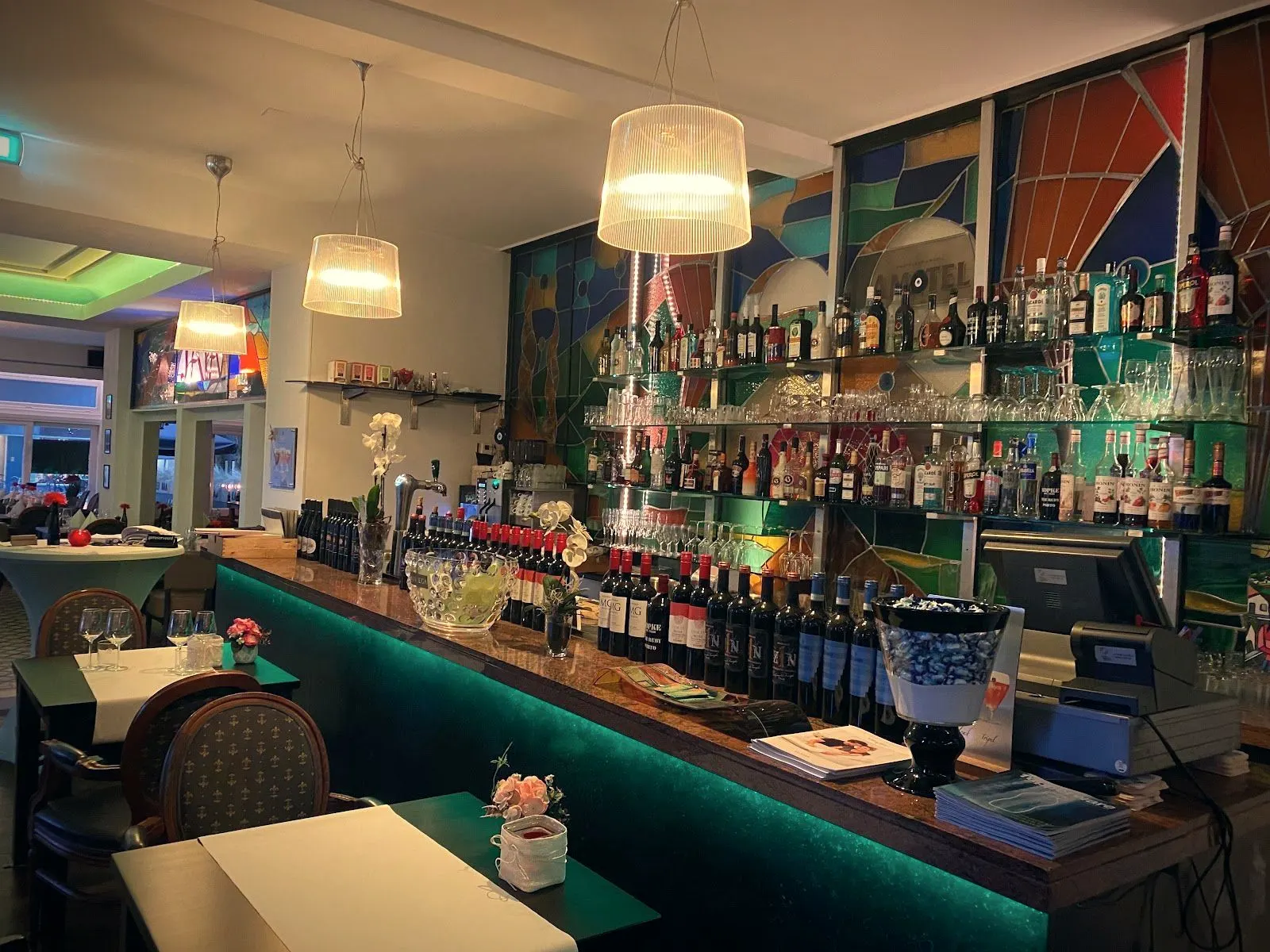 De bar met groen licht eronder en een wand van glas-in-lood erachter